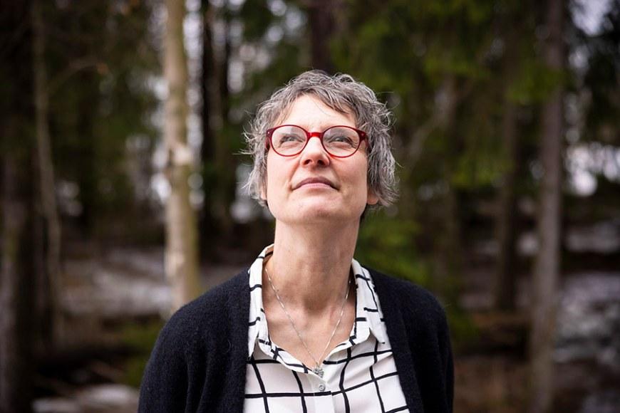 Katri Lindfors is standing in a forest landscape, looking up at the horizon.