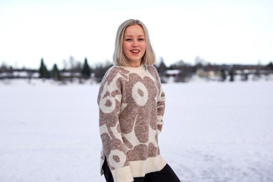 Jaara Jäntti seisoo lumisessa maisemassa harmaavalkoinen neule päällään.